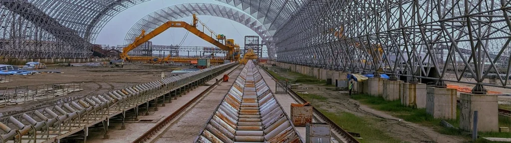 Bulk material handling system with heavy-duty conveyor idlers and rollers in a large industrial facility